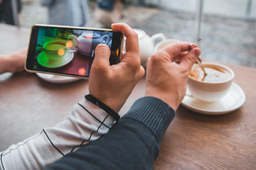 couple sitting in cafe drinking warm up tea in cold autumn day. woman taking picture on phone for...