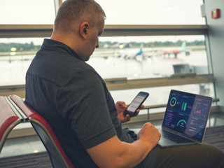 businessman sitting at airport with laptop and smartphone