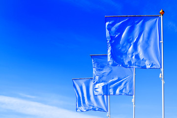Fototapeta na wymiar Blue flags waving in the wind against the cloudless sky. Perfect layout to add any logo, symbol or sign