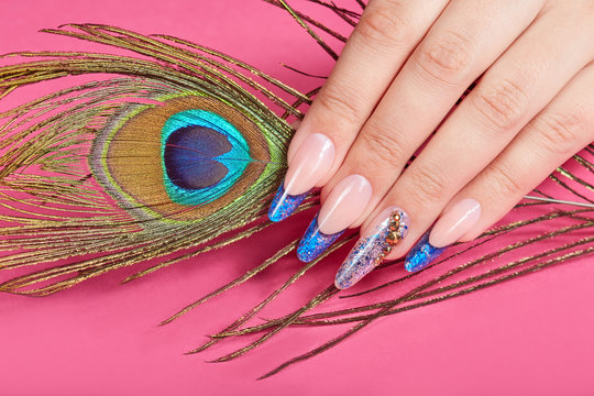 Hand with long artificial blue french manicured nails and peacock feather