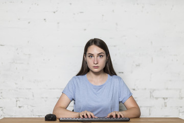 The girl stares straight. She sits at the table and works on computer.