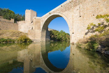 Fototapeta na wymiar horizontal shot of arch of Alcantara bridge, landmark and monument from ancient Roman age, reflected on water of river Tagus, Tajo in Spanish, in Toledo city, Spain, Europe