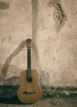 Classical nylon string guitar leaning against rough exterior wall at night. © Kevin Brine