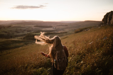 young woman with long hair walking through a field in england with a backpack