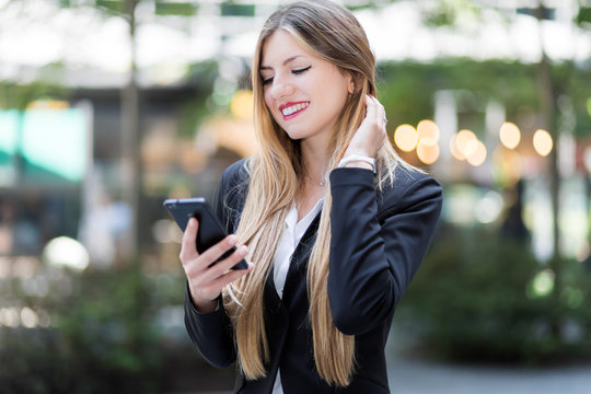 Young businesswoman using her smartphone to browse web content and sending messages outdoor