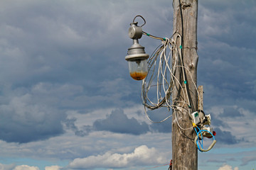Fototapeta premium Wooden pillar with old lantern and wires against the sky with clouds