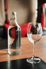Tall glass bottle of water and an empty glass on a wooden table