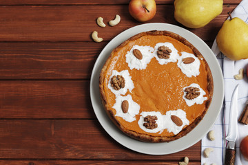 Sweet pumpkin pie close up on a brown wooden background. Pumpkin pie with whipped cream and nuts. Apples and pears. Place for text.