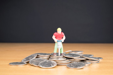 MINIATURE WORKER DRILLING IN PILE OF COINS