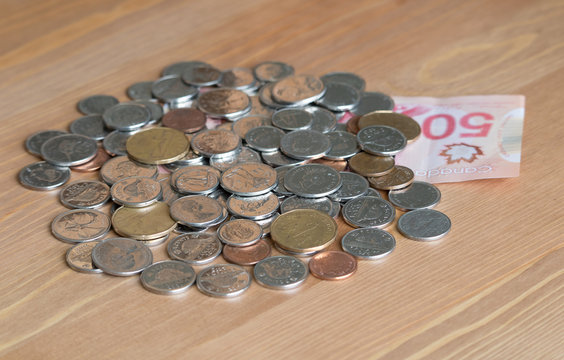 A pile of canadian coins and a canada dollar banknote on a wood background