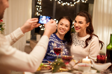 holidays and celebration concept - happy friends having christmas dinner at home and taking picture by smartphone