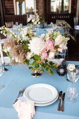 Festive table decorated with flowers and candles on a silver candlestick on blue tablecloth