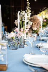 Long festive table with blue tablecloth decorated with flowers and candles