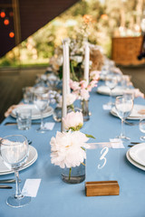 Long festive table with blue tablecloth decorated with flowers and candles
