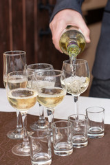 Man's hand pours champagne, white wine from bottle in wineglasses on table