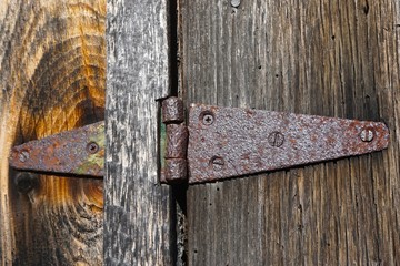 Close-up of a rusted hinge on the wooden door of an old barn.