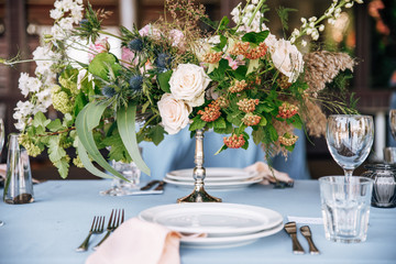 Festive table with blue tablecloth decorated with flowers in hight silver vase