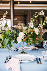 Festive table decorated with flowers and candles on a silver candlestick on blue tablecloth