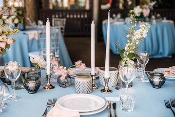 Festive table decorated with flowers and candles on a silver candlestick on blue tablecloth