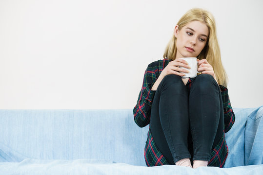 Sad lonely woman sitting on couch with mug