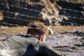 Athlete crawling under barbed wire at an obstacle course race 