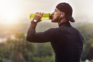 Fototapeta premium Muscular bearded athlete drink a water after good workout session on city park.