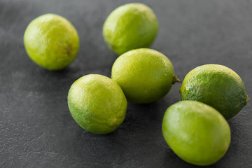 food, healthy eating and vegetarian concept - close up of whole limes on slate table top