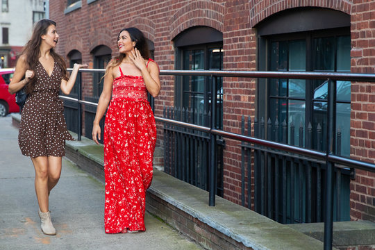 Two Female Friends Walking And Talking Outside On Sidewalk