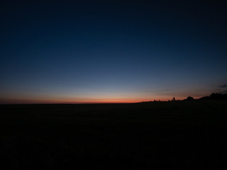Beautiful summer sunset over the field. Colored sky by the sunset. Orange sunset sky.