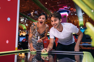 Happy couple playing coin operated air hockey game at a gaming p - obrazy, fototapety, plakaty