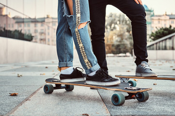 Leisure and sport concept - close-up photo of a trendy dressed teen couple with skateboards on street.