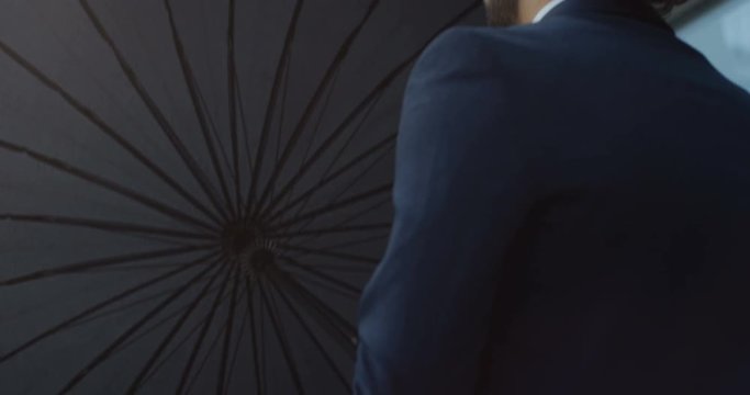 Close up of the back biew on the good looking Caucasian businessman opening his umbrella while walking as it raining. rear. Outside.