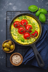 Frittata with arugula, potatoes and cherry tomatoes in iron pan on old stone table background. Top view.