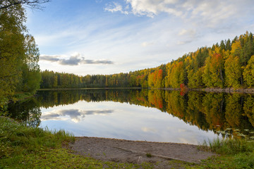 The most beautiful scenery on an autumn evening. Colorful forest and reflective water. Wallpaper with blue sky and reflection in the water.