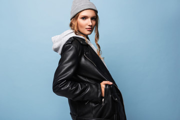 Beautiful girl with wavy hair in gray hat and black leather jacket dreamily looking in camera over...