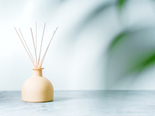 aroma reed diffuser home fragrance with rattan sticks on a light background with palm leaves and shadows.
