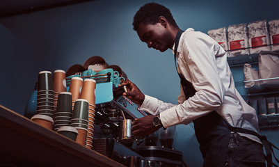 Side View of African American barista in white shirt and apron making coffee with a coffee machine.
