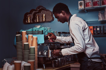 Side View of African American barista in white shirt and apron making coffee with a coffee machine.