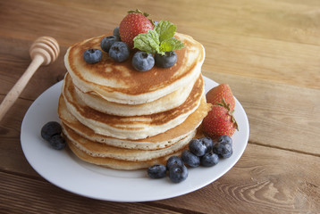 American pancakes with strawberry and blueberry jam, delicious dessert for breakfast, rustic style, wooden background. Copy space.