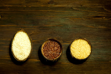 different types of rice in natural coconut bowls on wooden background. The concept of  tasty and healthy meal, copy space, closeup.