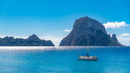 Ibiza, Cala d’Hort beach, beautiful sunny seascape with a sailboat and rocks in the sea
