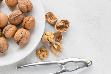 Walnuts on a white plate, cracked walnut next to and silver nutcracker