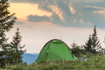 Small tourist tent on grassy mountain hill. Summer camping in mountains at dawn. Tourism concept.