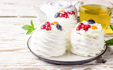 Delicious mini Pavlova meringue cake decorated with fresh red currant and blueberry
