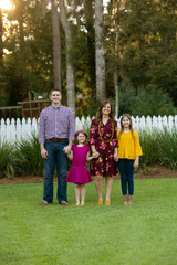 Family of Four Holding Hands Outside of Home with White Picket Fence