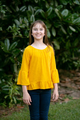 Fototapeta premium Smiling Tween Girl in Yellow Gold Outside in Greenery