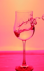 Close up view of splushing water in glass isolated. Pink background. Beautiful backgrounds.