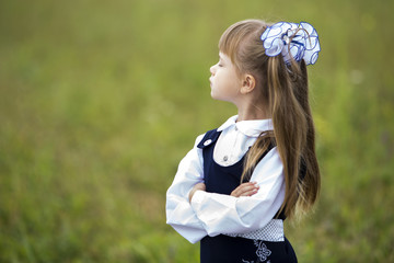 Profile portrait of cute adorable first grader girl in school uniform and white bows in long hair...
