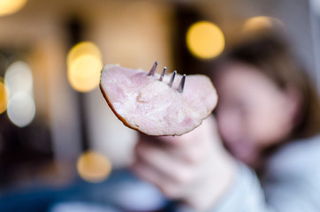 Adult holds up a piece of Canadian Bacon with a fork. Focus on the Canadian Bacon. Background intentionally blurred