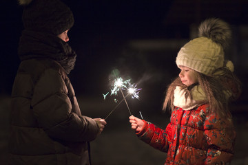 Profile of two cute young children, boy and girl in warm winter clothing holding burning sparkler...